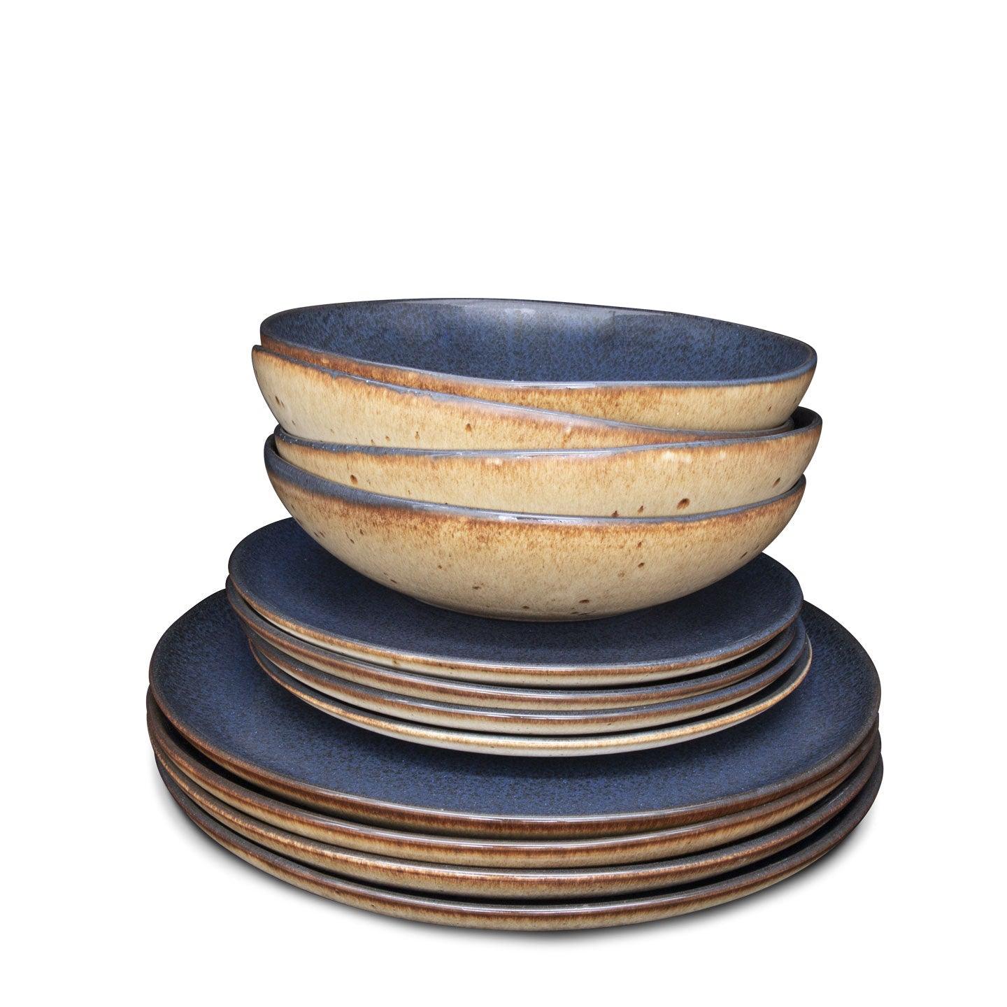 A stack of artisanal blue and beige speckled ceramic plates and bowls on a white background.